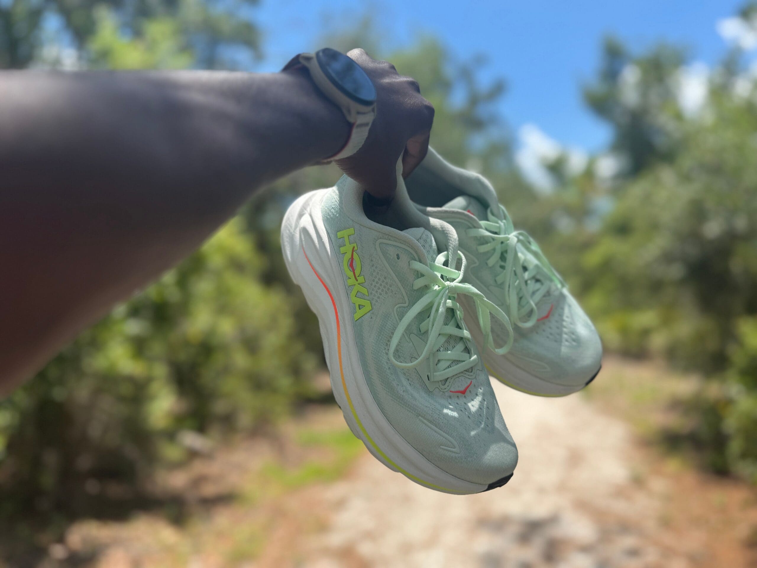 HOKA clifton 10s in hand with trail in background