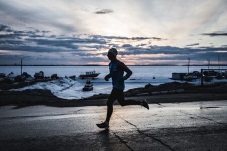 6 Best Winter Running Shoes (2026): Snow, Ice, & Sub-Freezing Miles man running in the winter on an icy road with winter running gear