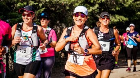 6 Best Running Shoes for Supination & Underpronation (2026) A group of smiling women running together in a race wearing hydration vests and race bibs on an outdoor trail