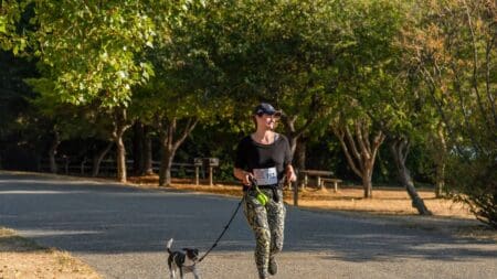 How to Start Running With Your Dog: Tips for Safety, Form, & Endurance Woman running with her dog on a leash in a sunny park path