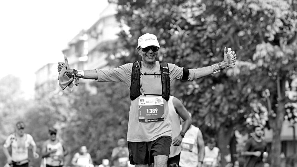 Running Is the Most Expensive Free Hobby: Where All Your Money Goes Smiling marathon runner wearing a hydration vest, race bib, sunglasses, and GPS watch on an outdoor race course