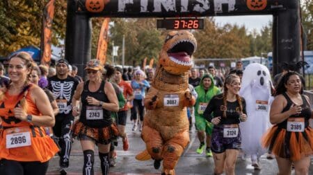 22 Best Inflatable Costumes for a Halloween 5K: Funny, Viral & Completely Unhinged Runner in an inflatable T-Rex costume and runners in Halloween outfits crossing a 5K race finish line arch