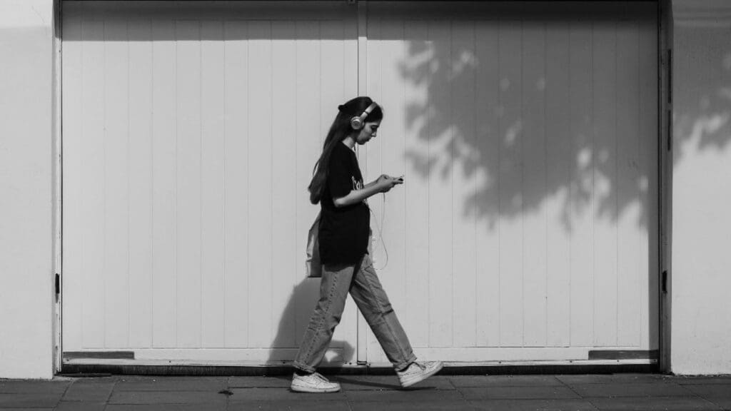 How Many Miles Can You Walk Listening to Sarah J. Maas Books? Black and white photo of a woman wearing over-ear headphones walking along a sidewalk while listening to an audiobook on her phone